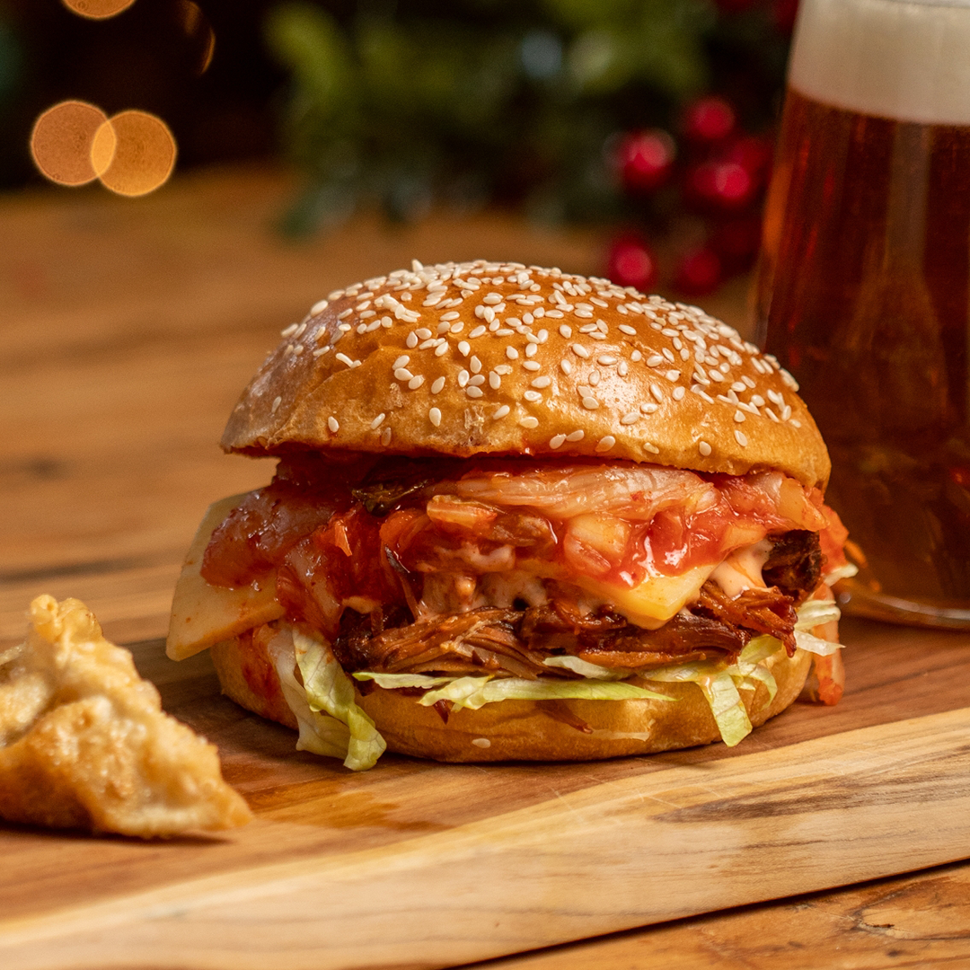 A delicious kimchi burger with gochujang mayo, melted cheese, juicy meat, fresh salad, and tangy kimchi stacked between a soft bun.